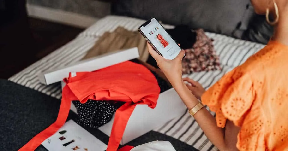 A customer looking up a new dress on the Ellegra app and having other clothes on her bed from Ellegra.