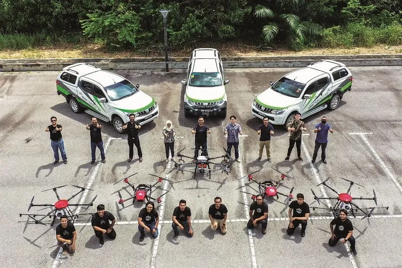 A picture of the team of Aerodyne Group and their fleet of drones and company cars in the background.